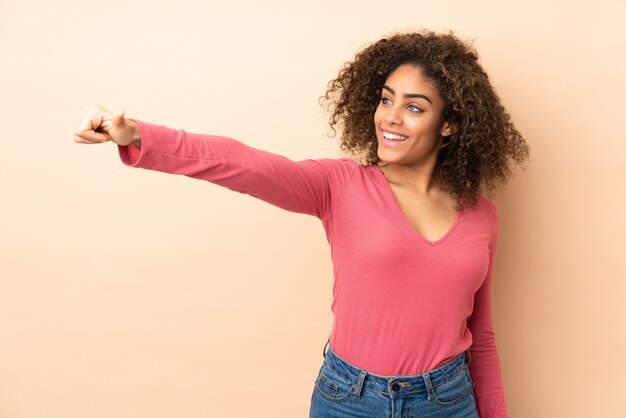 Young African American woman on beige wall giving a thumbs up gesture