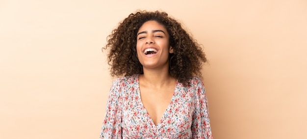 Young African American woman on beige wall laughing