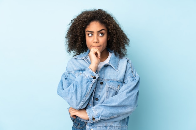 Young African American woman on blue wall having doubts and thinking