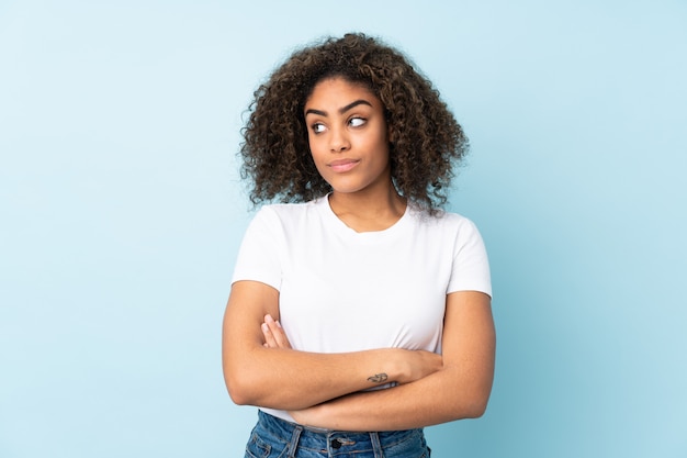 Giovane donna afro-americana sulla parete blu mantenendo le braccia incrociate