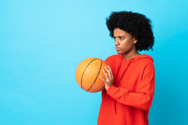 Young african american woman on blue wall playing basketball