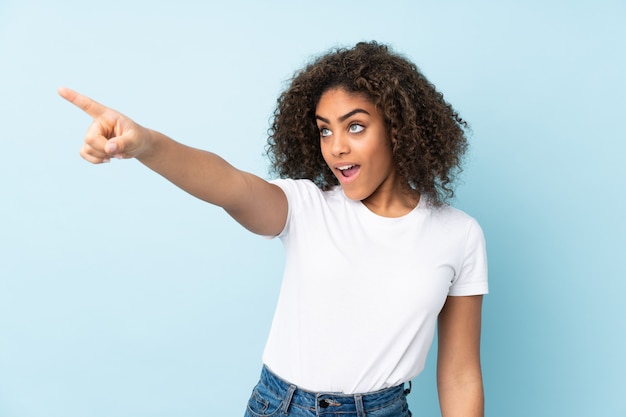 Young African American woman on blue wall pointing away