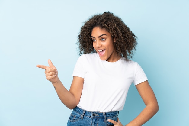 Young African American woman on blue wall pointing finger to the side