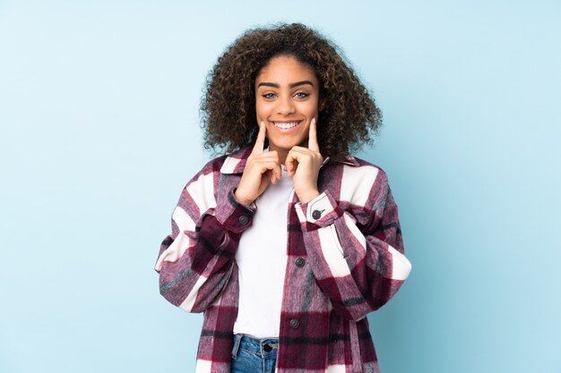 Young African American woman on blue wall smiling with a happy and pleasant expression