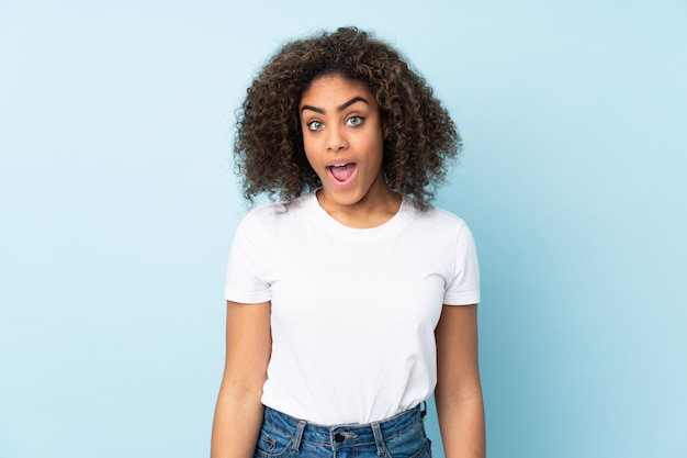 Young African American woman on blue wall with surprised facial expression