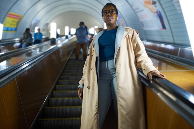 Young African American woman in casualwear standing on escalator and moving downwards