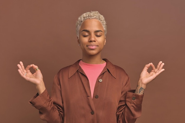 Young african american woman closes eyes during meditation or\
yoga in studio