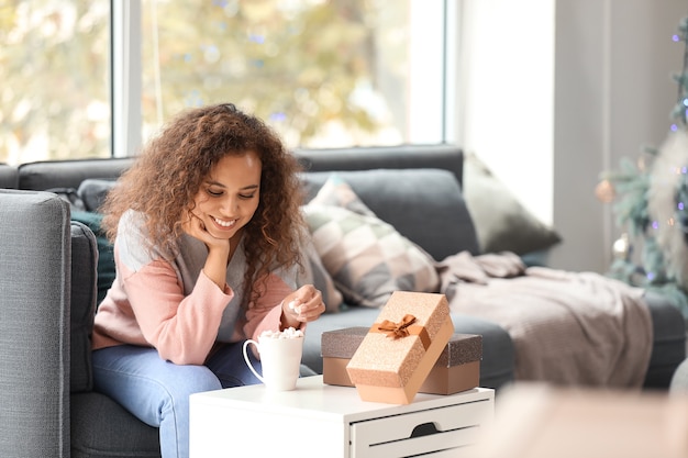 Young African-American woman drinking hot chocolate at home on Christmas eve