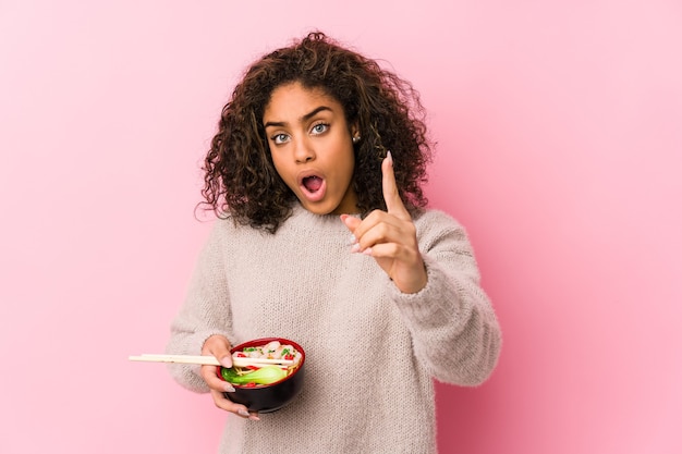 Young african american woman eating noodles having an idea, inspiration concept.