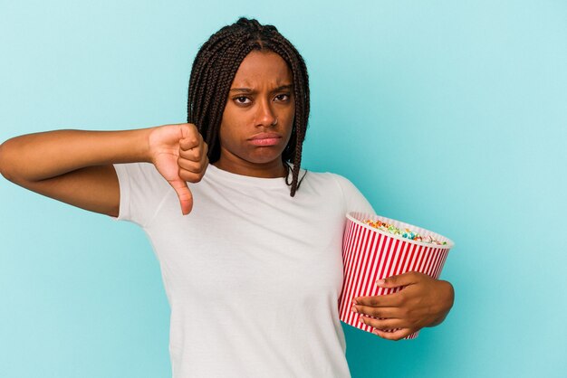 Young African American woman eating pop corns isolated on blue background  showing a dislike gesture, thumbs down. Disagreement concept.