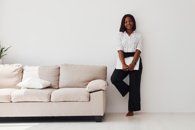 Молодая африканская американка в формальной одежде стоит с ноутбуком в руках в помещении