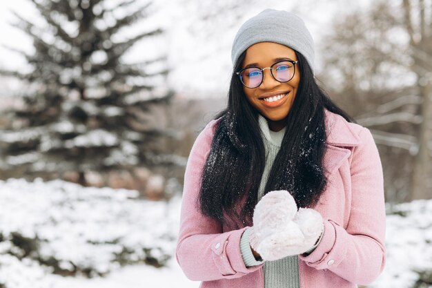 雪の中で遊ぶ眼鏡と暖かい手袋の若いアフリカ系アメリカ人女性