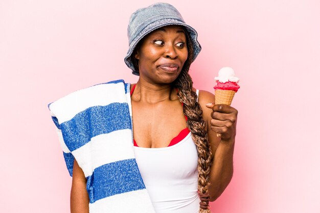 Young African American woman going the beach holding an ice cream isolated on pink background