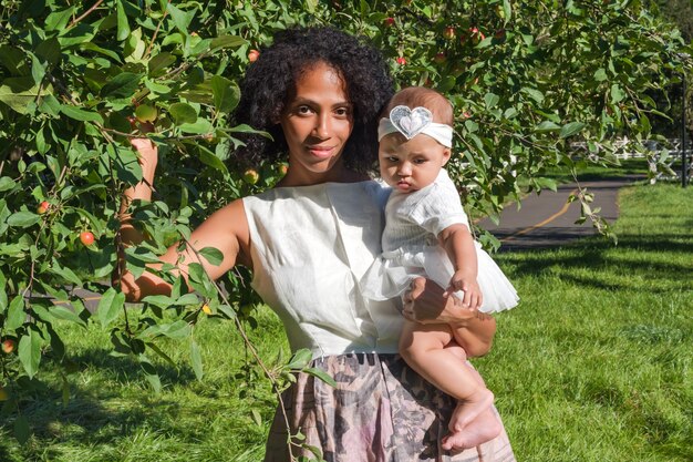 Young african american woman and her daughter smiling walking in summer park.