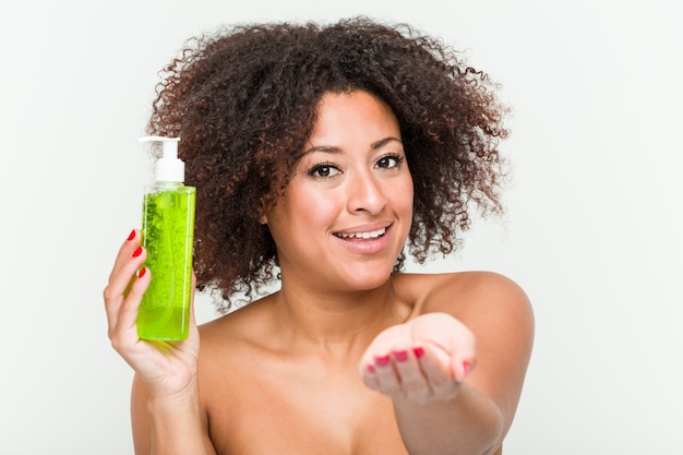 Young african american woman holding aloe vera bottle pointing with finger at you as if inviting come closer.