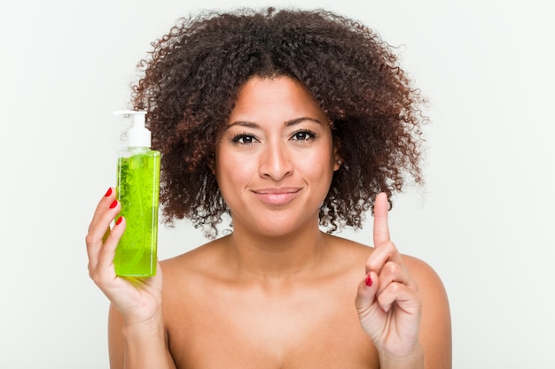 Young african american woman holding aloe vera bottle showing number one with finger.