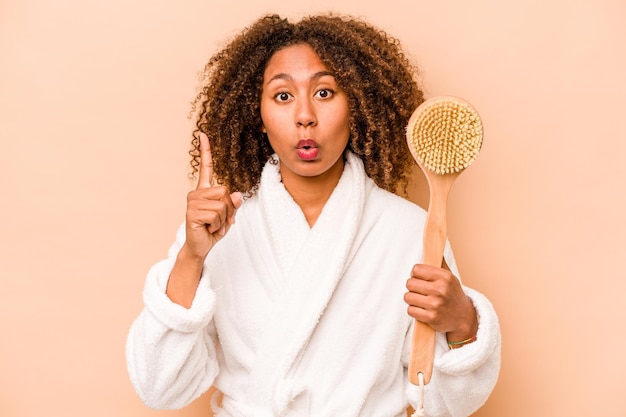 Photo young african american woman holding back scratcher isolated on beige background having some great idea concept of creativity