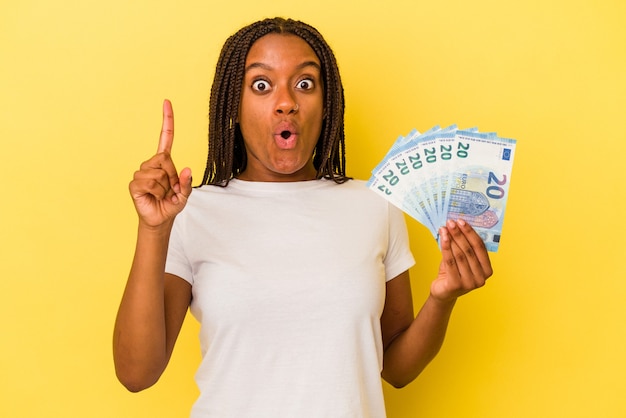 Young african American woman holding bills isolated on yellow background  having some great idea, concept of creativity.