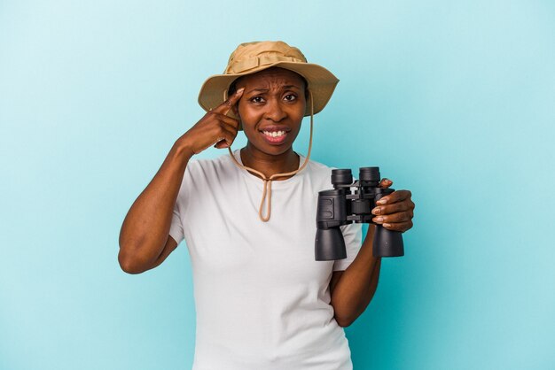 Young african american woman holding binoculars isolated on blue background showing a disappointment gesture with forefinger.