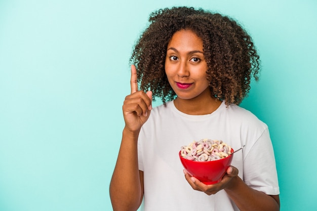 Young african american woman holding a bowl of cereals isolated on blue background showing number one with finger.