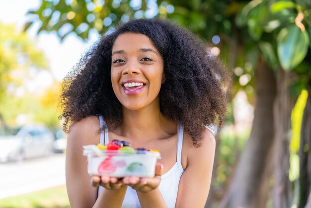 アフリカ系アメリカ人の若い女性が屋外で果物のボウルを握っている