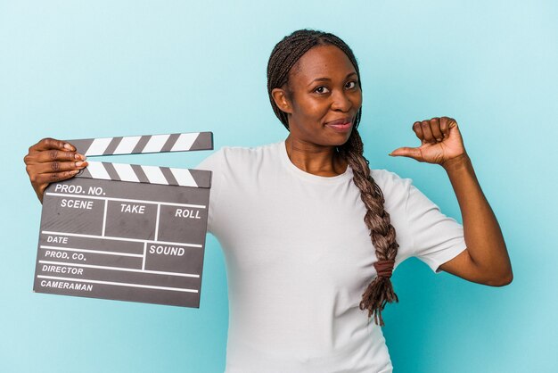 Young african american woman holding clapperboard isolated on blue background feels proud and self confident, example to follow.