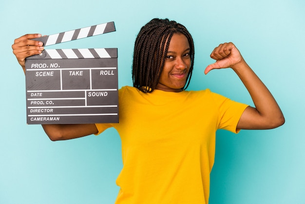 Young african american woman holding a clapperboard isolated on blue background  feels proud and self confident, example to follow.