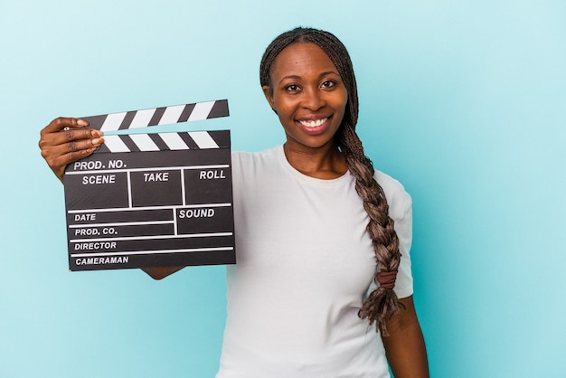 Young african american woman holding clapperboard isolated on blue background happy, smiling and cheerful.