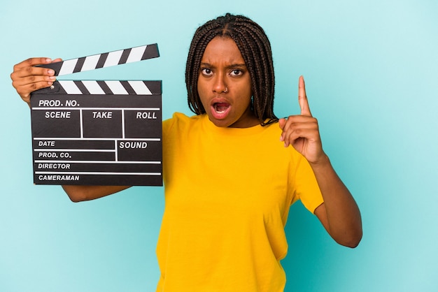 Young african american woman holding a clapperboard isolated on blue background  having an idea, inspiration concept.