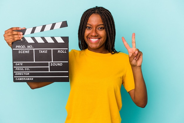 Young african american woman holding a clapperboard isolated on blue background  showing number two with fingers.