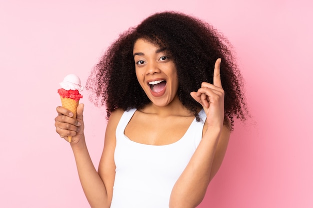 Young african american woman holding a cornet ice cream on pink wall pointing up a great idea