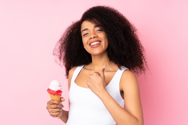 Young african american woman holding a cornet ice cream on pink wall with thumbs up because something good has happened