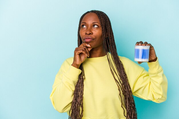 Young african american woman holding cotton bulls isolated on buds background looking sideways with doubtful and skeptical expression.