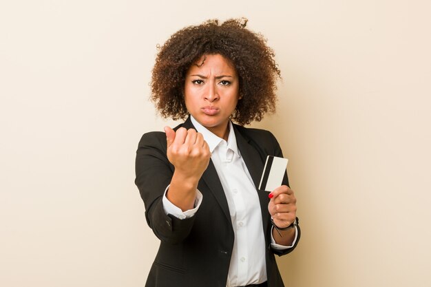 Young african american woman holding a credit card showing fist to camera, aggressive facial expression.