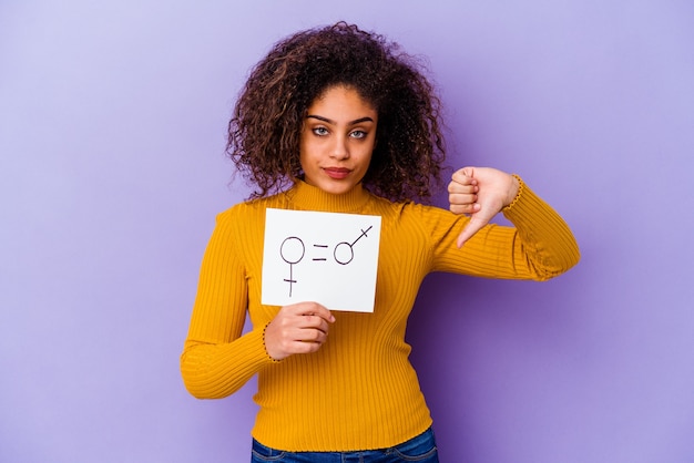 Young African American woman holding a gender equality placard isolated on purple wall showing a dislike gesture, thumbs down. Disagreement concept.
