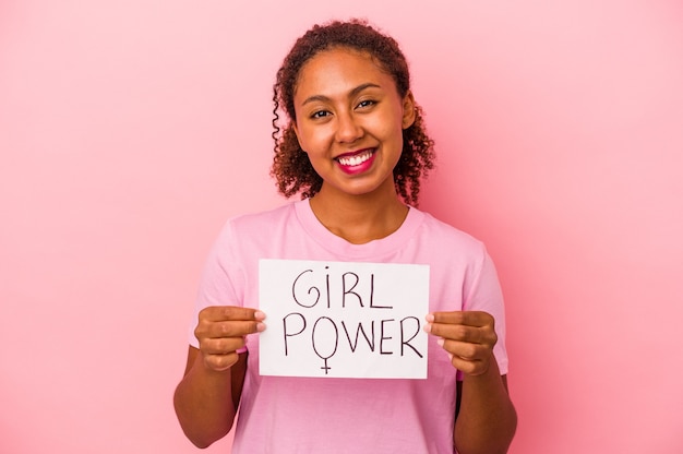 Young African American woman holding a girl power placard isolated on pink background