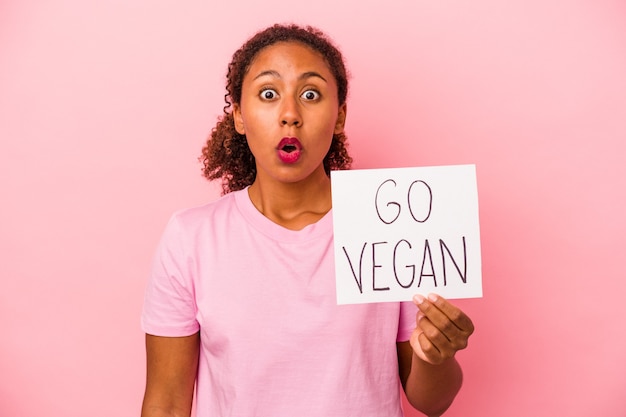 Young African American woman holding a go vegan placard isolated on pink background