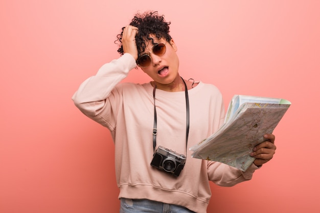 Young african american woman holding a map being shocked, she has remembered important meeting.