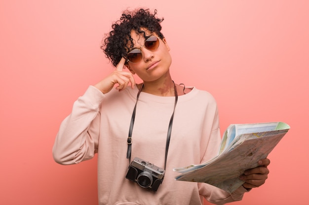 Young african american woman holding a map pointing his temple with finger, thinking, focused on a task.