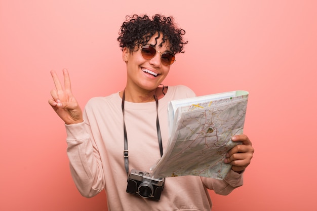 Young african american woman holding a map showing number two with fingers.