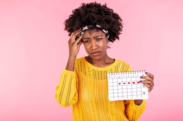 Photo young african american woman holding menstruation calendar over isolated background with surprise face woman holding menstruation calendar with confused face afraid and excited with fear expression