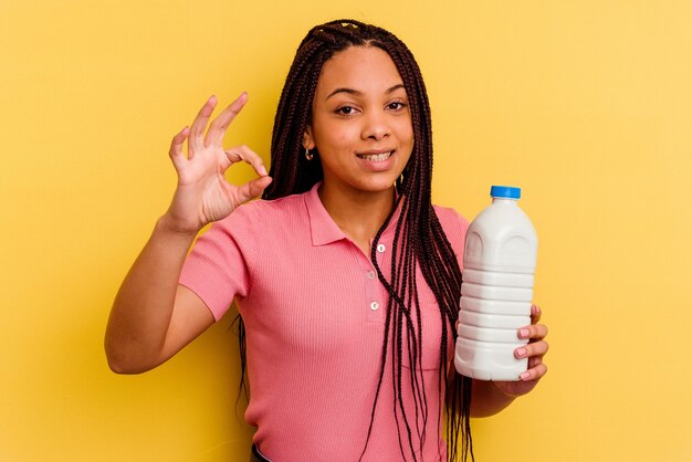 노란색 벽 명랑 하 고 확신 보여주는 확인 제스처에 고립 된 우유 병을 들고 젊은 아프리카 계 미국인 여자.