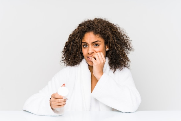 Young african american woman holding a moisturizer biting fingernails, nervous and very anxious.