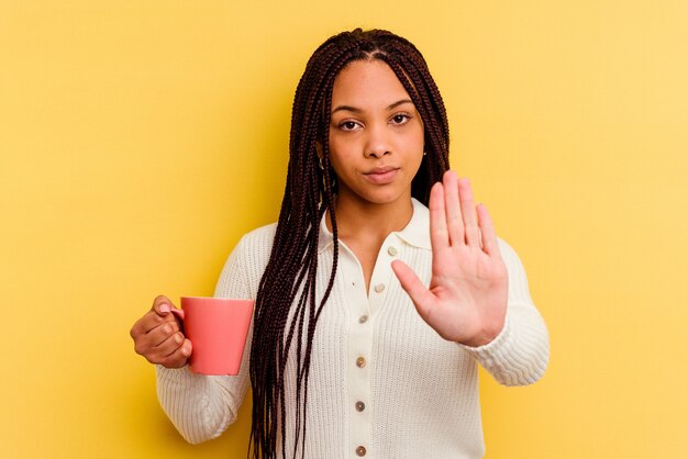 Foto giovane donna afroamericana che tiene una tazza isolata in piedi con la mano tesa che mostra il segnale di stop, impedendoti.