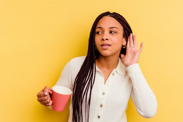 Young african american woman holding a mug isolated trying to listening a gossip.