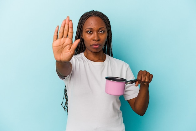 Young african american woman holding pan isolated on blue background standing with outstretched hand showing stop sign, preventing you.