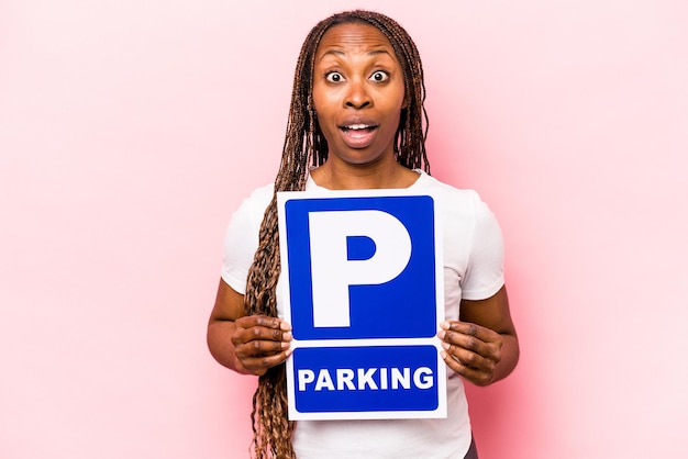 Young African American woman holding parking placard isolated on pink background