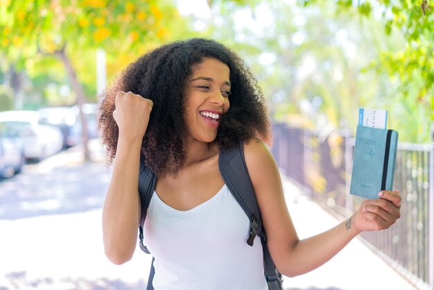 Young African American woman holding a passport at outdoors celebrating a victory