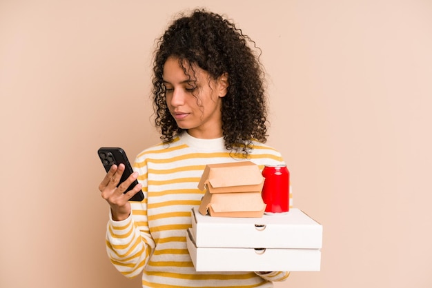 Young african american woman holding a pizza and burger fast food calling with mobile phone isolated