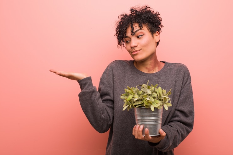 Photo young african american woman holding a plant impressed holding blank space on palm.